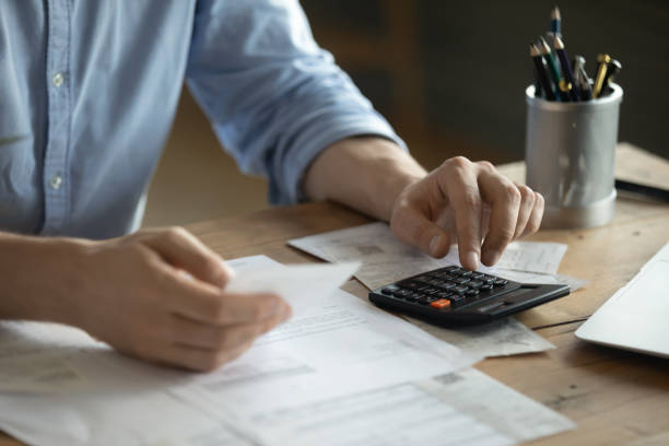 Man sitting at table using calculator calculates costs manage budget Personal finance management, accounting concept. Close up view man sitting at table using calculator performs arithmetic operations calculates costs per month, manage family budget, control expenses vat stock pictures, royalty-free photos & images