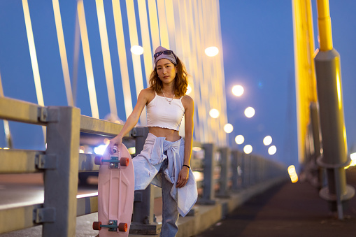 Portrait young Asian beautiful woman holding skateboard on the bridge