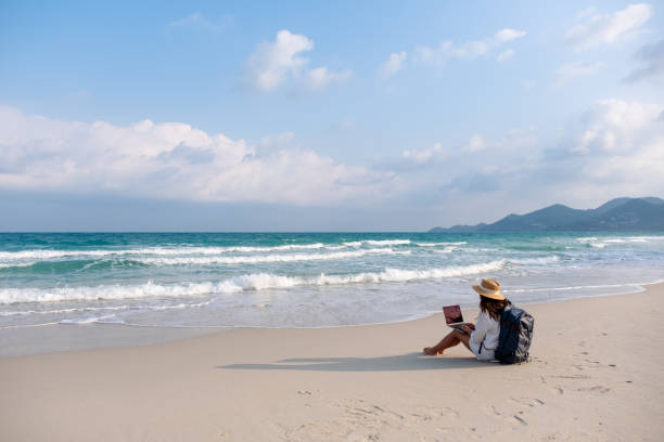 istock A female traveler using and working on laptop computer while sitting on the beach 1306235566