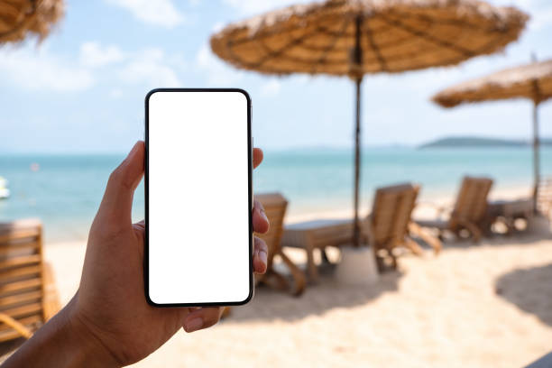 istock a man holding mobile phone with blank desktop screen while sitting on the beach 1306235571