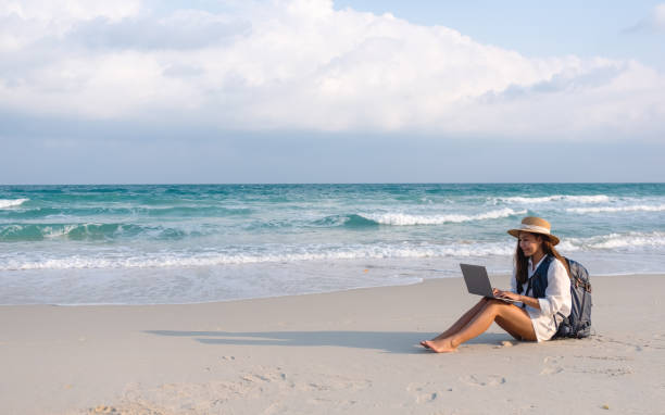 istock A female traveler using and working on laptop computer while sitting on the beach 1306235588