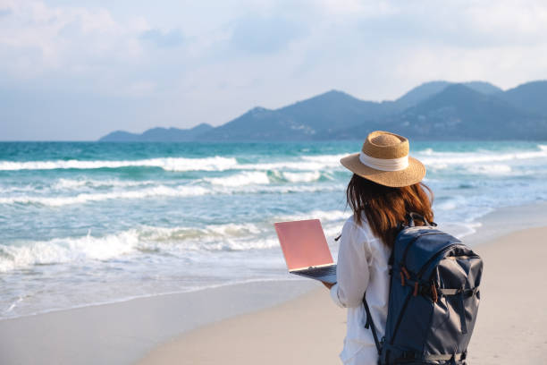 istock A young female traveler using and working on laptop computer while walking on the beach 1306235621