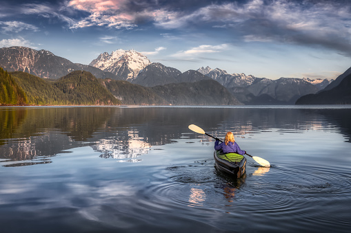 Adventurous Girl kayaking on an infatable kayak in a beautiful lake. Colorful peaceful Sunrise Art Render. Taken in Stave Lake, East of Vancouver, British Columbia, Canada. Adventure and vacation