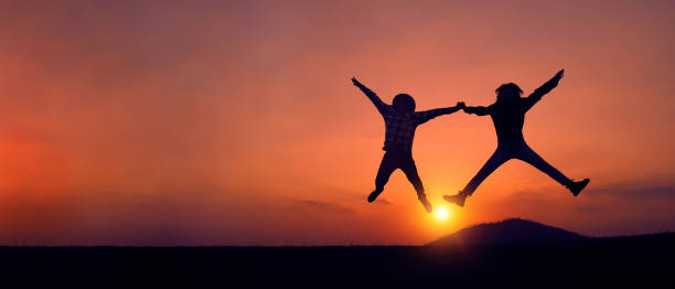 istock Silhouette of two people jumping joyfully at sunset. 1306240180