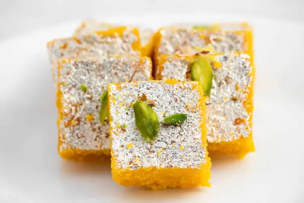Photo of Famous Indian Mithai Moong Dal Burfi Barfee Or Meetha Mung Daal Barfi Made Of Yellow Gram Flour In Desi Ghee Mixed With Mawa Pistachio And Khoya. Isolated On White Background With Space For Text