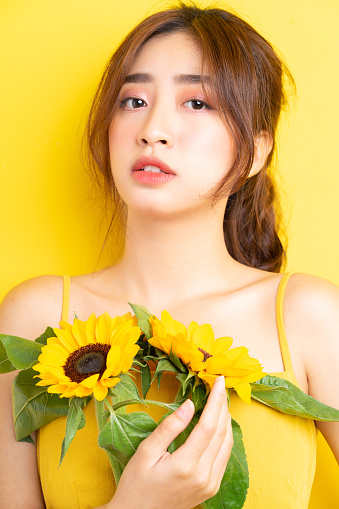 Beautiful Asian woman holding and posing with sunflower on yellow background