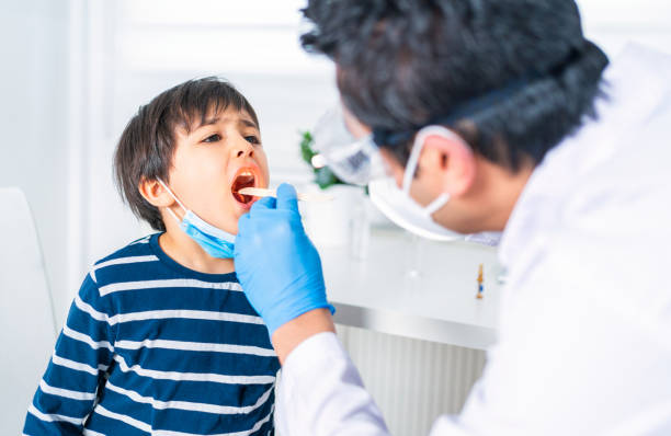 pédiatre mâle examinant la gorge du petit patient d’enfant à la clinique - doctor patient male tongue depressor photos et images de collection