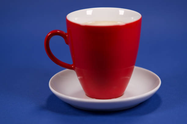 Organic coffee creamer is being poured into a freshly brewed cup of black coffee. The coffee mug, as well as the table setting and background are all white.