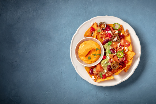 Nachos with chili con carne, guacamole and cheese, top shot on a blue background with a place for text