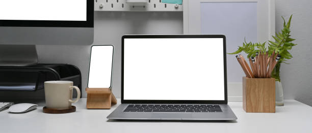 istock Horizontal image of modern workplace with smart phone, laptop and computer pc on white table. 1306251990