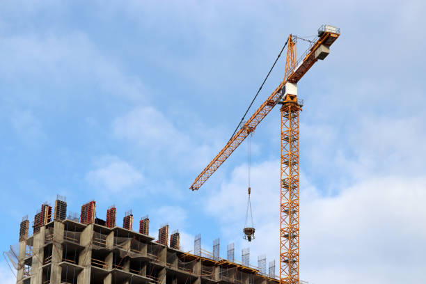 istock Construction crane lifting the cargo above unfinished residential building on blue sky and white clouds background 1306252685