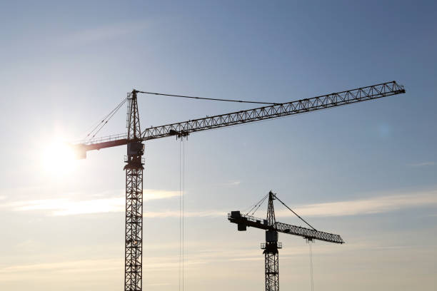 istock Silhouettes of two construction cranes on blue sky and sunshine background 1306253036