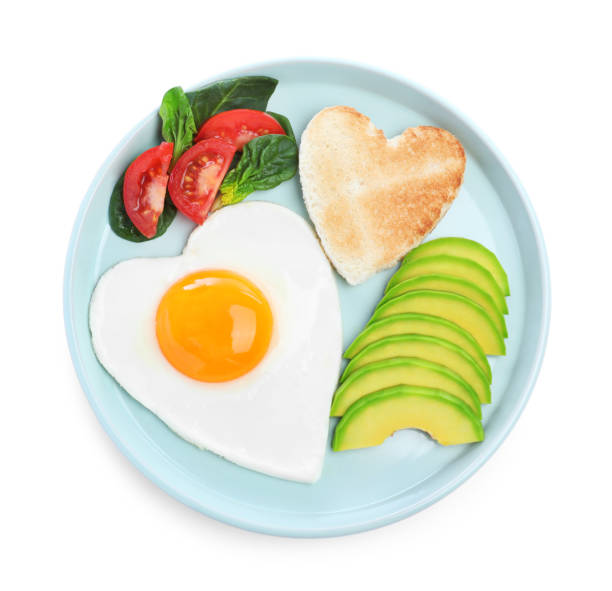 istock Romantic breakfast with fried heart shaped egg, avocado and toast isolated on white, top view. Valentine's day celebration 1306255589