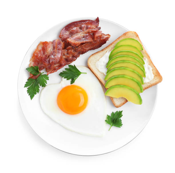 istock Romantic breakfast with fried bacon, heart shaped egg and avocado toast isolated on white, top view. Valentine's day celebration 1306255646