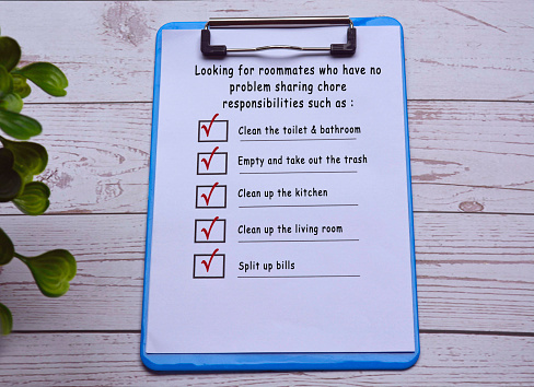 Text on blue clip board with pen on wooden desk. Finding roommate checklist