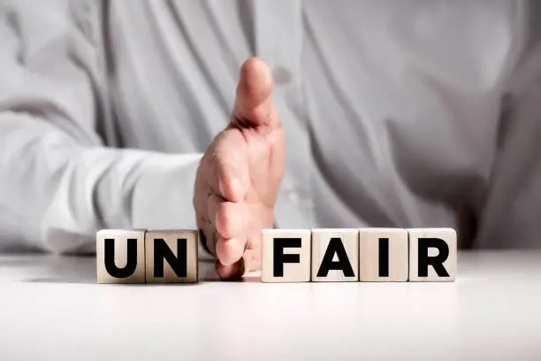 Businessman hand puts away the first two letters from the word unfair and transforms it into fair. Justice and fairness in business concept.