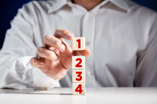 Businessman hand puts a wooden block with the number one on top of the tiered cubes. First step, level or rank