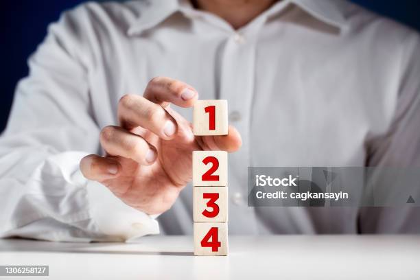 Businessman Hand Puts A Wooden Block With The Number One On Top Of The Tiered Cubes First Step Level Or Rank Stock Photo - Download Image Now