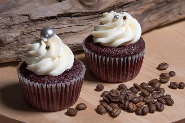 Two cupcakes on wooden background and white coffee cup, homemade cake with cream and roasted coffee beans.