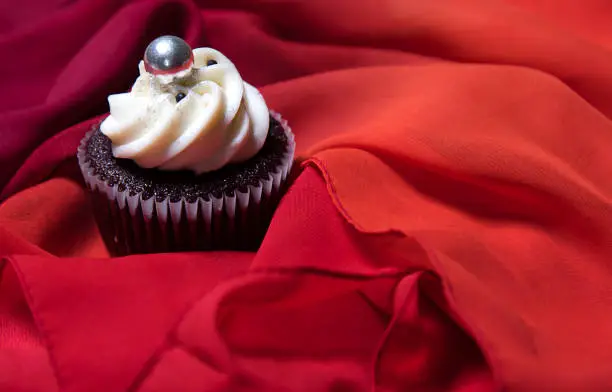 Ð¡upcake on red fabric background, homemade chocolate cake with white cream