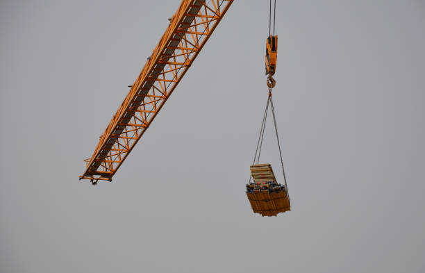 크레인에는 강철 로프에 묶인 용기가 있는데, 이 용기는 흔들리고 돌이 빠져나왔습니다. 건설 현장에 추락할 위험이 있습니다. 자재의 수직 수송없이 건설 작업 - crane hook industry picking up 뉴스 사진 이미지