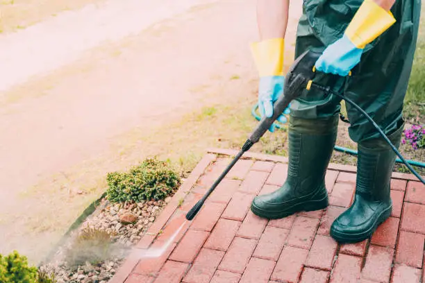 Photo of Man cleaning red, conrete pavement block using high pressure water cleaner. Paving cleaning concept