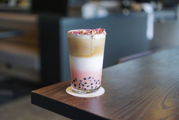 Rose tea Coffee Latte with tapioca pearl. A beautiful three Layer of rose tea, milk and coffee shot topped with dry rose and served with boba on the wooden table. bubble tea photos stock pictures, royalty-free photos & images