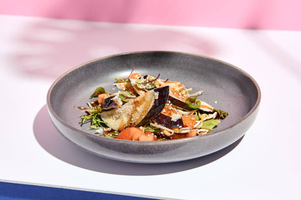 istock Eggplant restaurant appetizer plate. Restaurant appetizer food plate on white table with pink wall. Day sunlight with hard shadow of monstera palm leaves. Summer or spring restaurant food concept. 1306261160