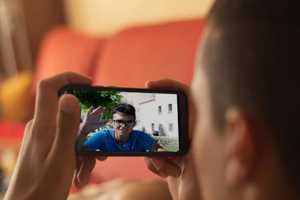istock selective focus videoconference of two young people made by the mobile one lying on the couch at home and another young man in the middle of nature in a rural environment 1306261877