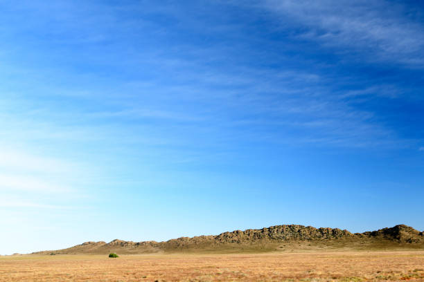 Rocky outcrop on grassy plain with soft clouds in blue sky