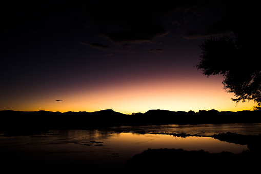 Dusk light over silhouetted mountains reflected on flowing river