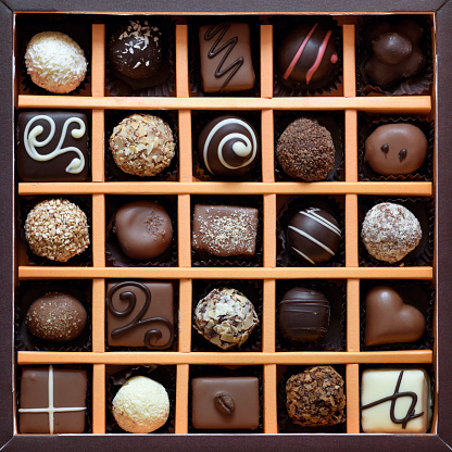 Close up color image depicting a box of gourmet chocolate truffles of different shapes and different varieties of chocolate. Selective focus with room for copy space.