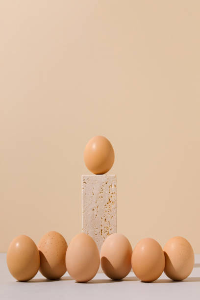 istock Single egg standing on a travertine marble block stage surrounded by group of eggs on a beige and gray background. 2021 Easter unique still life composition. Surreal retro creative food concept. 1306264884