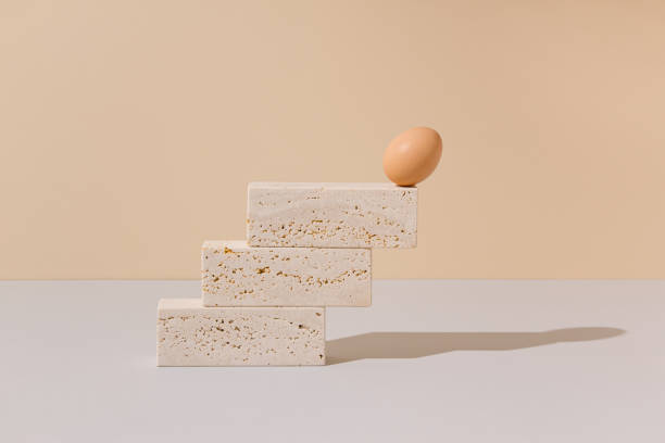 istock Single egg leaning on the edge of a travertine marble blocks steps on a beige and gray background. 2021 Easter unique still life composition. Surreal retro creative idea. 1306264885