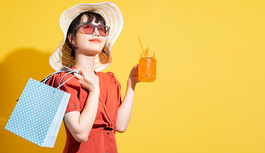 Young Asian businesswoman holding shopping bags posing on yellow background