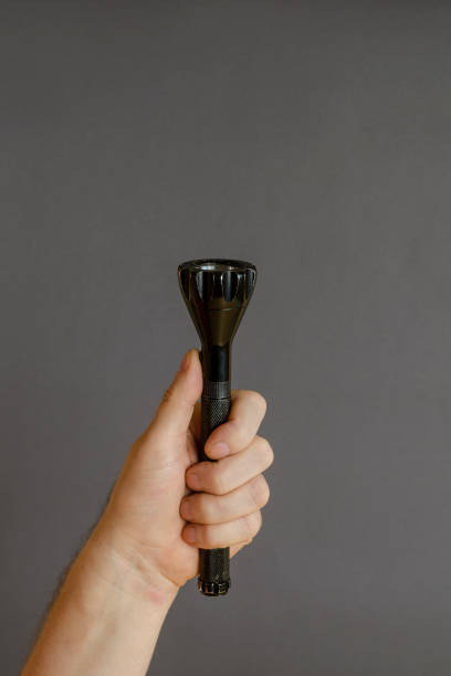 istock A hand holds a black modern LED flashlight on a gray background. 1306267215