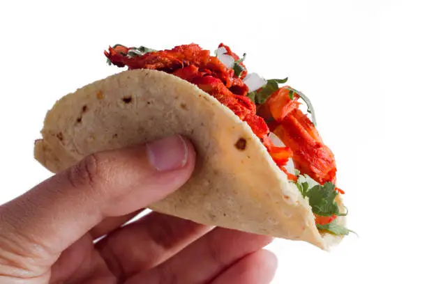 Photo of Close-up of a hand holding authentic mexican taco al pastor on a white background