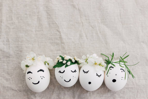 istock Happy Easter! Natural eggs with drawn funny faces in cute floral crowns top view on linen fabric 1306274619