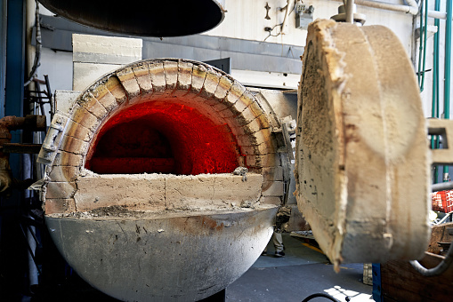 Partial view of opening to metal melting furnace on foundry floor.