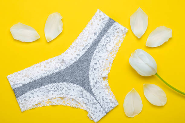 Breathable cotton gray panties for women and white tulip petals on a yellow background. Sexy lingerie with lace in tanga shape. Personal hygiene concept, aromatherapy, vaginal infection prevention. stock photo