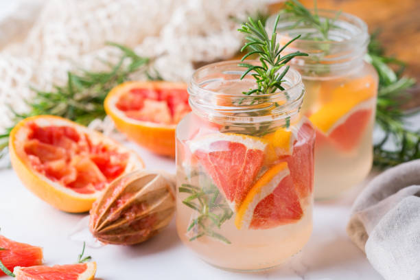 Hard seltzer cocktail with grapefruit and rosemary Hard seltzer cocktail with grapefruit, rosemary and ice on a table. Summer refreshing beverage, drink on a white table soda water glass lemon stock pictures, royalty-free photos & images