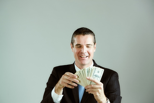 Man wearing a suit and tie counts a fistful of money in US dollar banknotes.