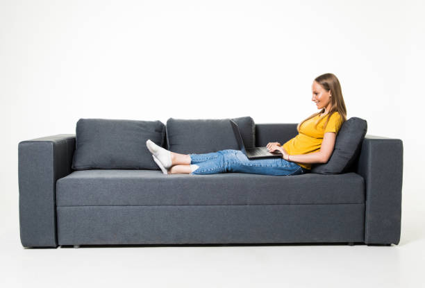istock Woman lying on sofa at home working on laptop isolated on white background. 1306289433