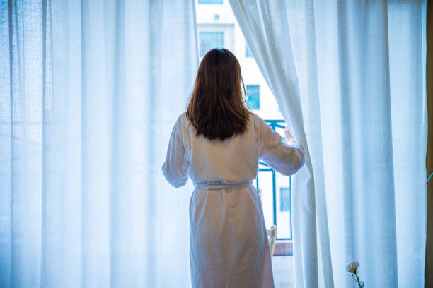 istock Young woman in bathrobe open curtains 1306289805