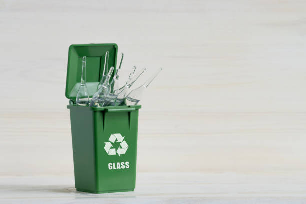 istock Green container for sorting garbage, with an open lid, glass ampoules and an ecology icon. Close-up, white wooden isolated background. The concept of sorting garbage, waste, for further processing 1306293705