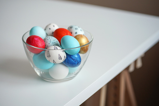 Colorful Easter eggs in transparent glass bowl on white table. Copy space, Easter concept. Hand-painted eggs
