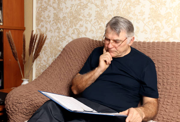 istock A man sits on the couch at home, works with documents, examines and reads postage paper documents, a serious man with glasses works remotely at home. 1306301783