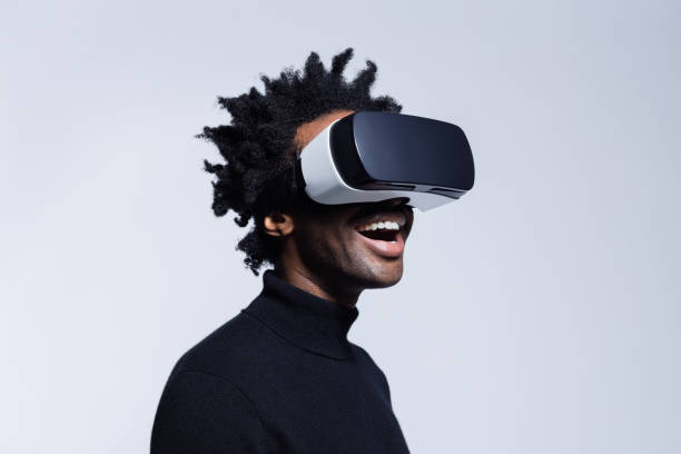 Happy young man using virtual reality glasses Portrait of excited afro american man wearing virtual reality glasses, standing against grey background. simulator stock pictures, royalty-free photos & images