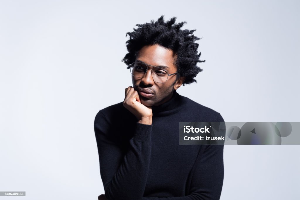 Portrait do man wearing turtleneck Confident afro american young man wearing black turtleneck and glasses, looking away with hand on chin. Studio shot on grey background. 25-29 Years Stock Photo
