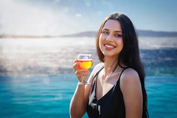 Portrait of an attractive woman with long, black hair enjoying a drink by the sea